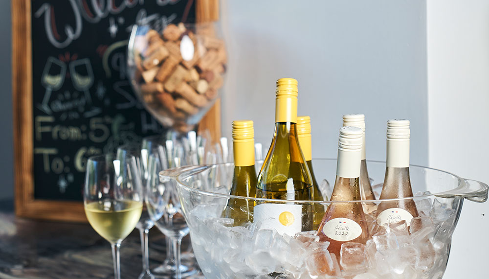 Bucket of ice with wine bottles with wine glasses and a glass of corks next to it